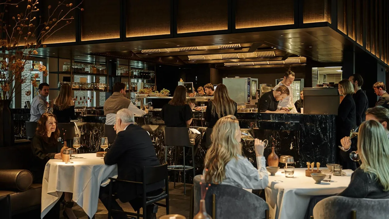 Guests dining at the busy brasserie with a backlit bar behind them.