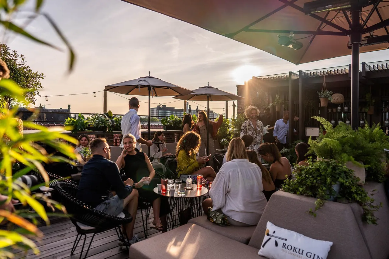 Guests relaxing under parasols on the rooftop terrace at sunset.