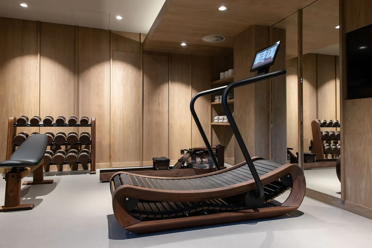 The wood-panelled gym with a curved treadmill and dumbbells.
