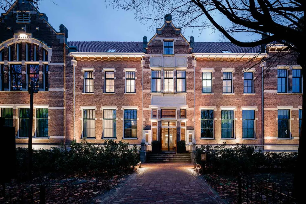 The illuminated hotel facade and entrance path at dusk.