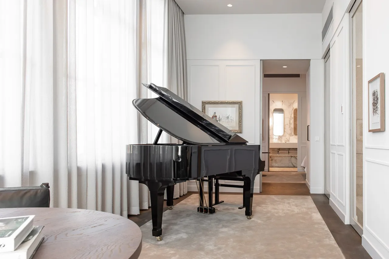 A grand piano in a light suite with long white curtains.