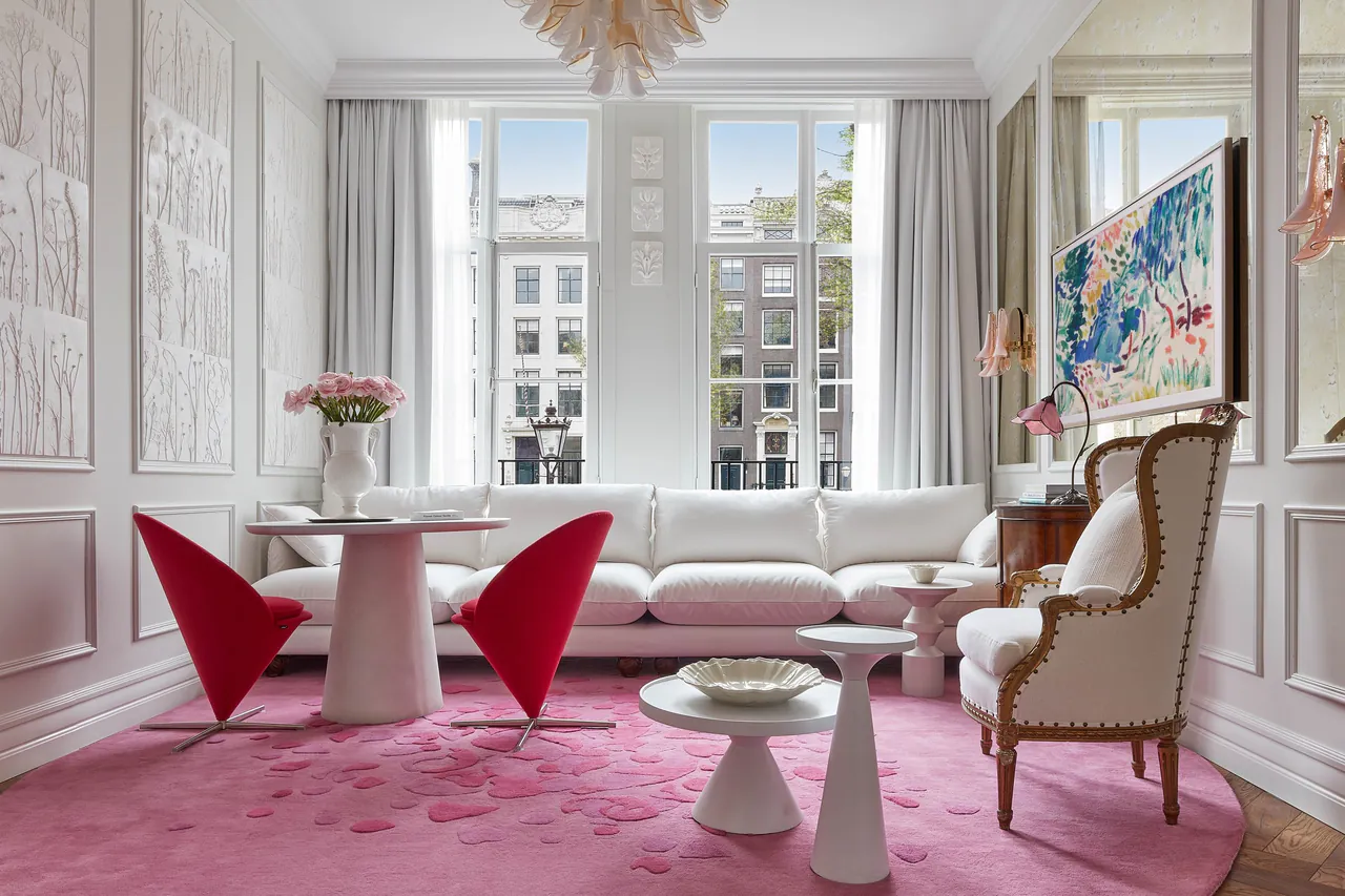 The bright living room of the Flower Collector's Suite with a pink rug and red chairs.