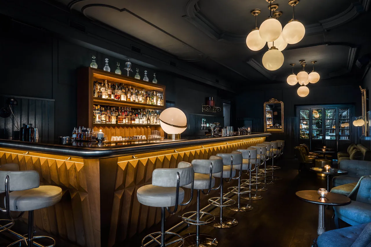 Pulitzer's Bar with a long lit counter, globe lamps and dark walls.
