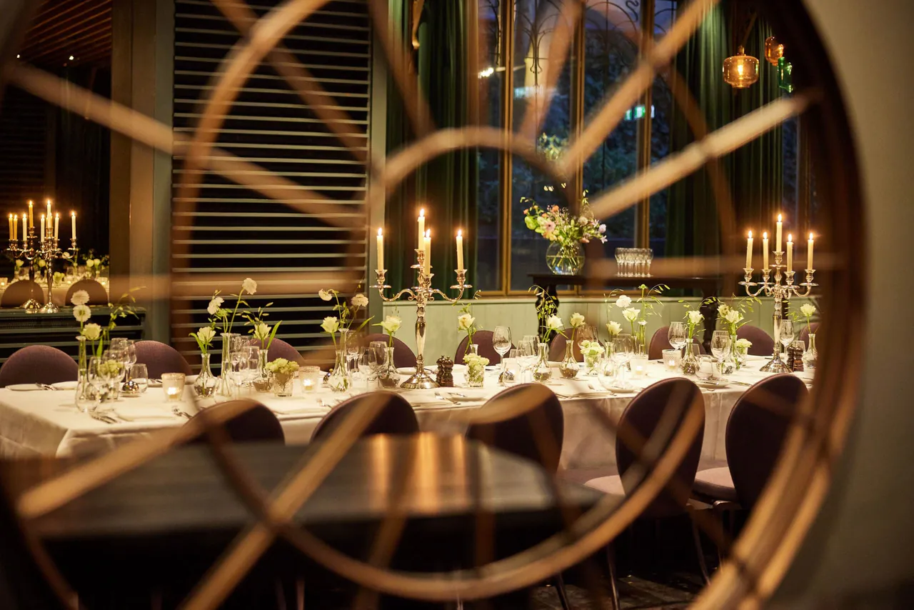A candlelit dinner table in the Garden Room seen through a round window.