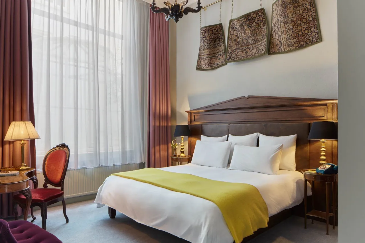 A bedroom in the Antique Collector's Suite with a carved headboard and yellow throw.