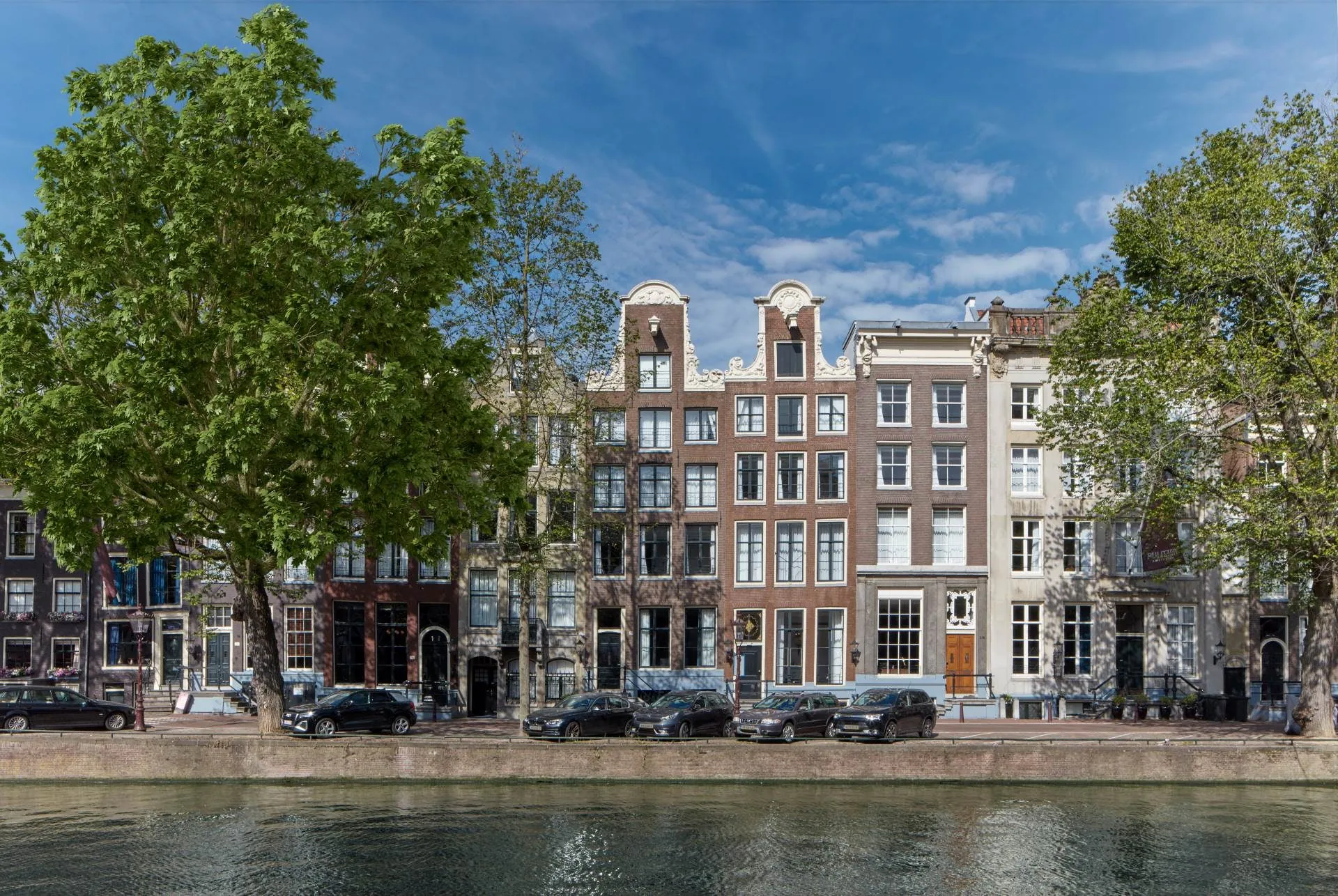 The row of historic canal houses that forms Pulitzer Amsterdam, seen across the water.