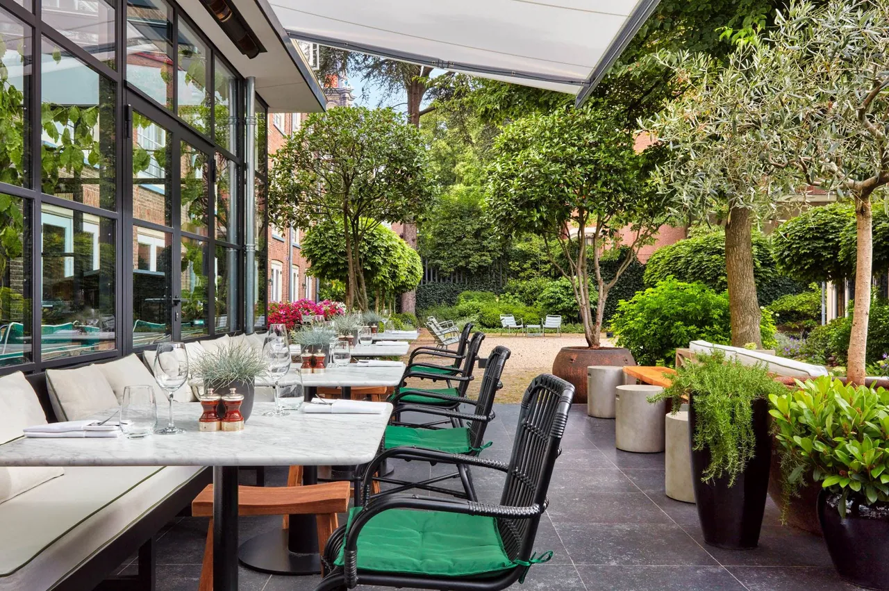 The garden terrace with laid tables beside the glass walls of the restaurant.