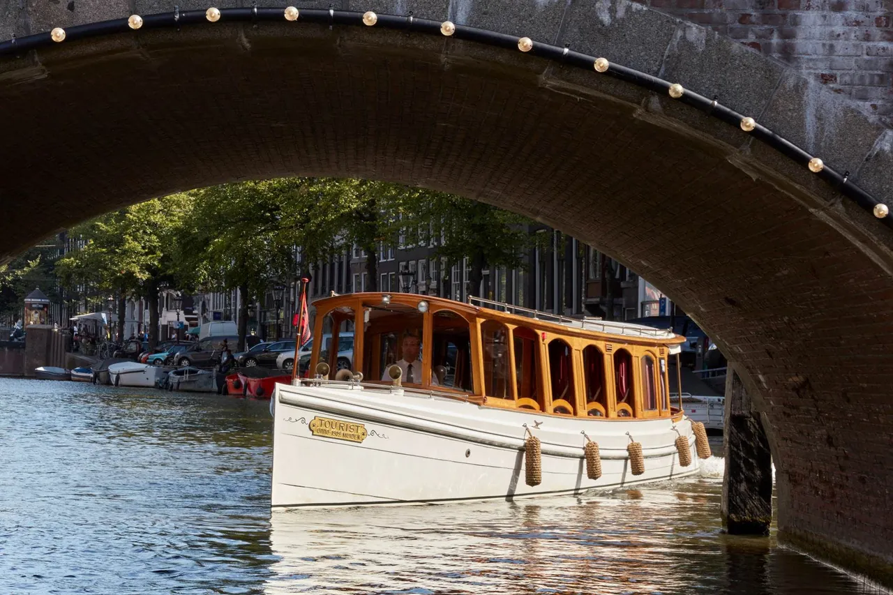 The hotel's classic salon boat passing under a canal bridge.