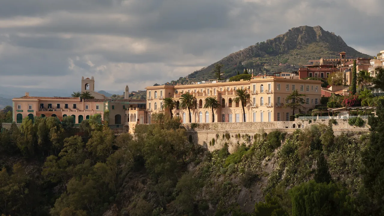 San Domenico Palace on its clifftop at the edge of Taormina, with the mountain rising behind it.