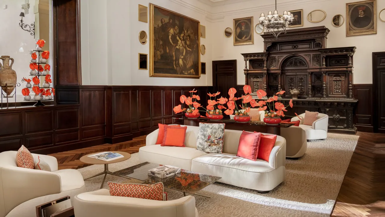 A lounge with white sofas, coral cushions, dark wood panelling and old paintings.