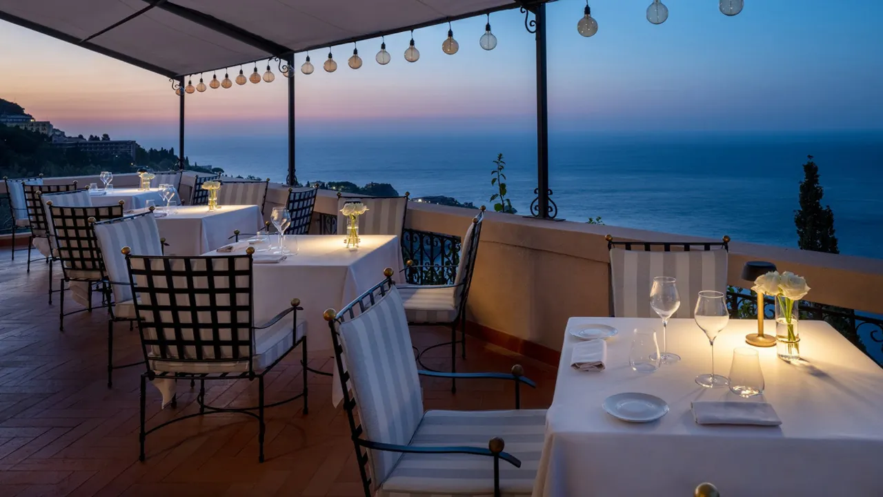 Tables set on the terrace at dusk, with the sea stretching out below.