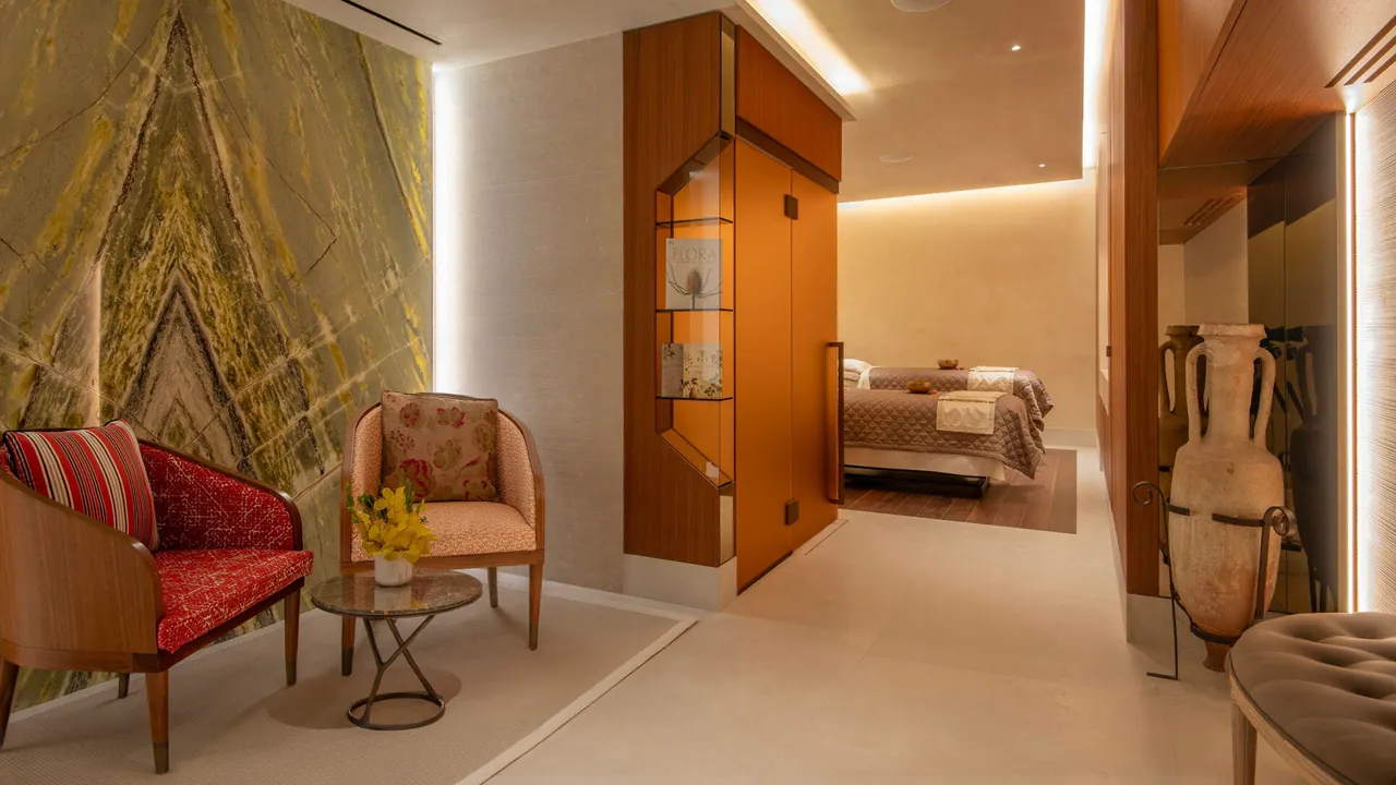 A spa lounge with a green marble wall, two armchairs and a treatment room beyond.
