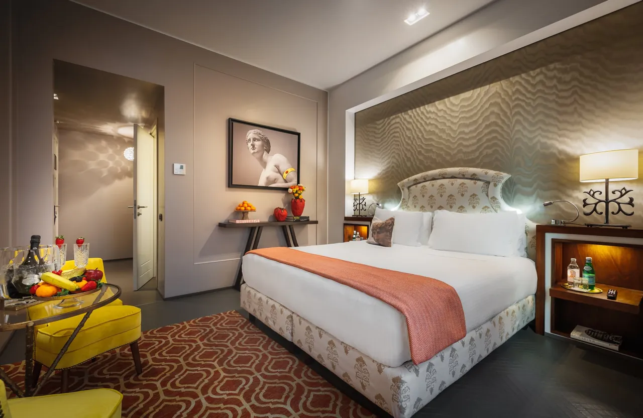 A superior room with a cream headboard, coral throw and colourful patterned rug.