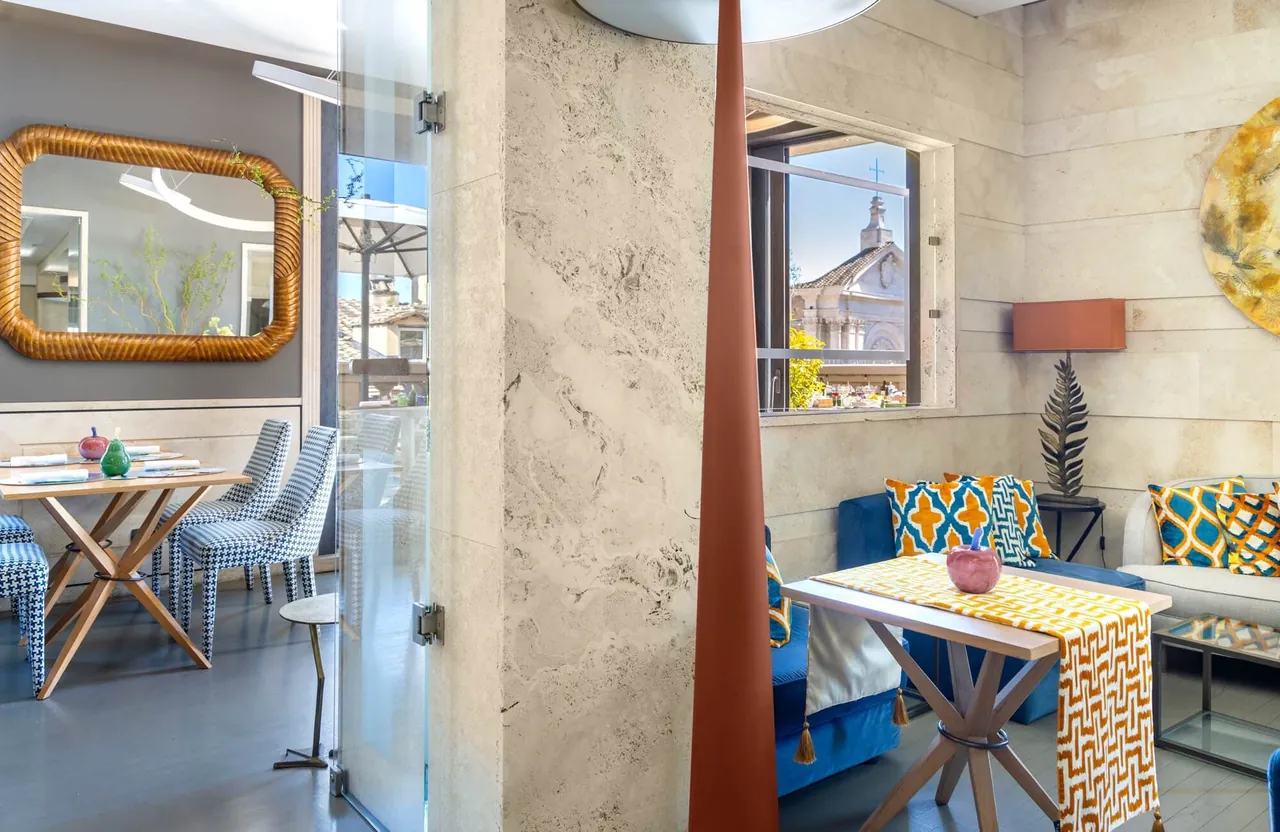A glass partition opening onto a sunny sitting room with a table and city views.