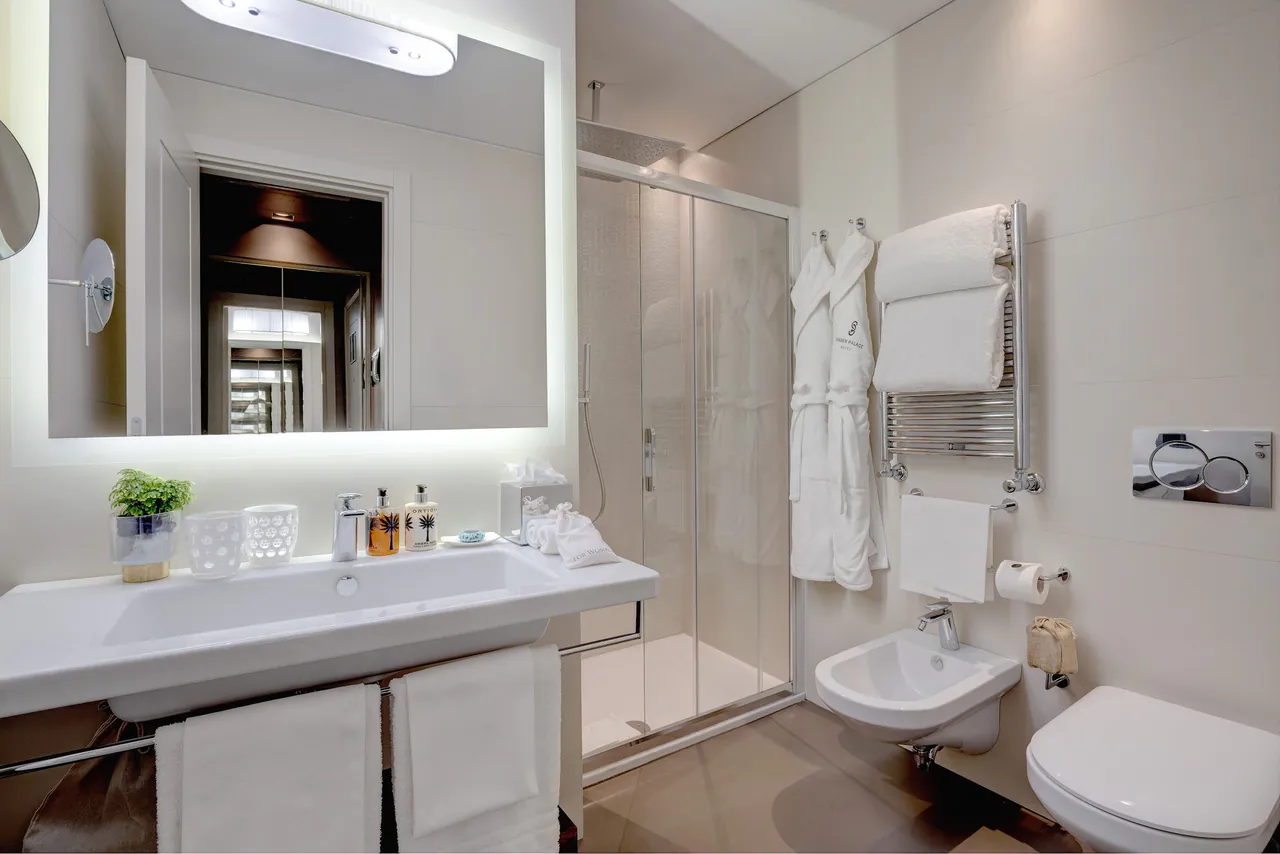 A white bathroom with a walk-in shower, backlit mirror and fluffy bathrobes.