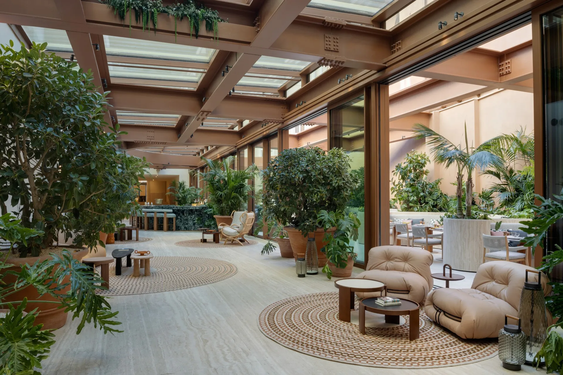 A glass-roofed courtyard lounge filled with plants, armchairs and woven rugs.