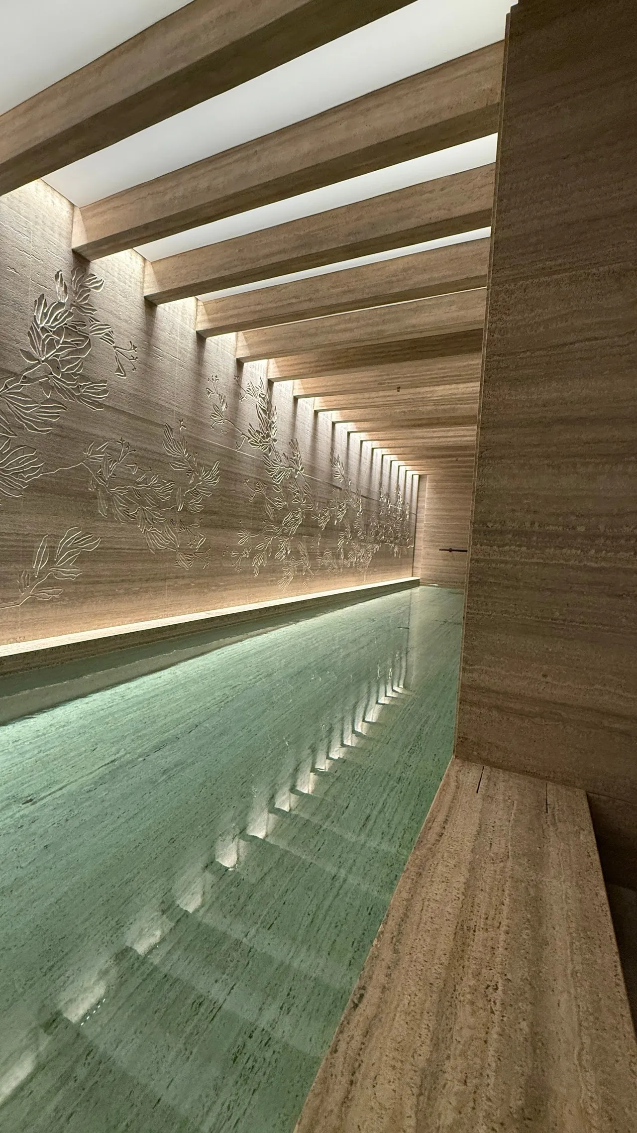 A long, softly lit indoor pool framed by stone walls and wooden beams.