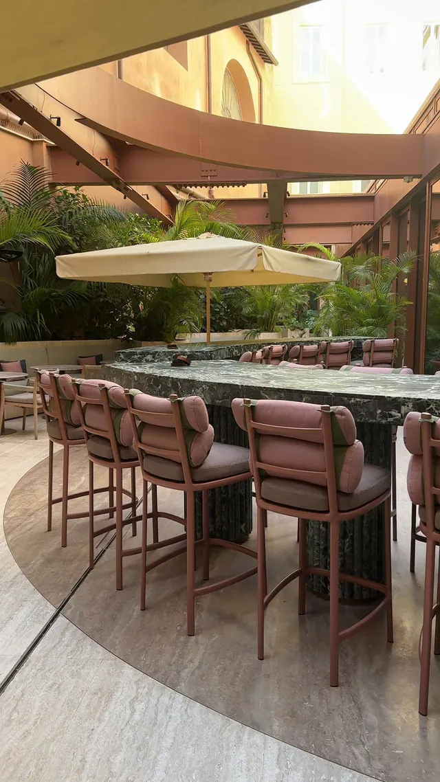 An outdoor bar with high stools beneath umbrellas and ochre walls.