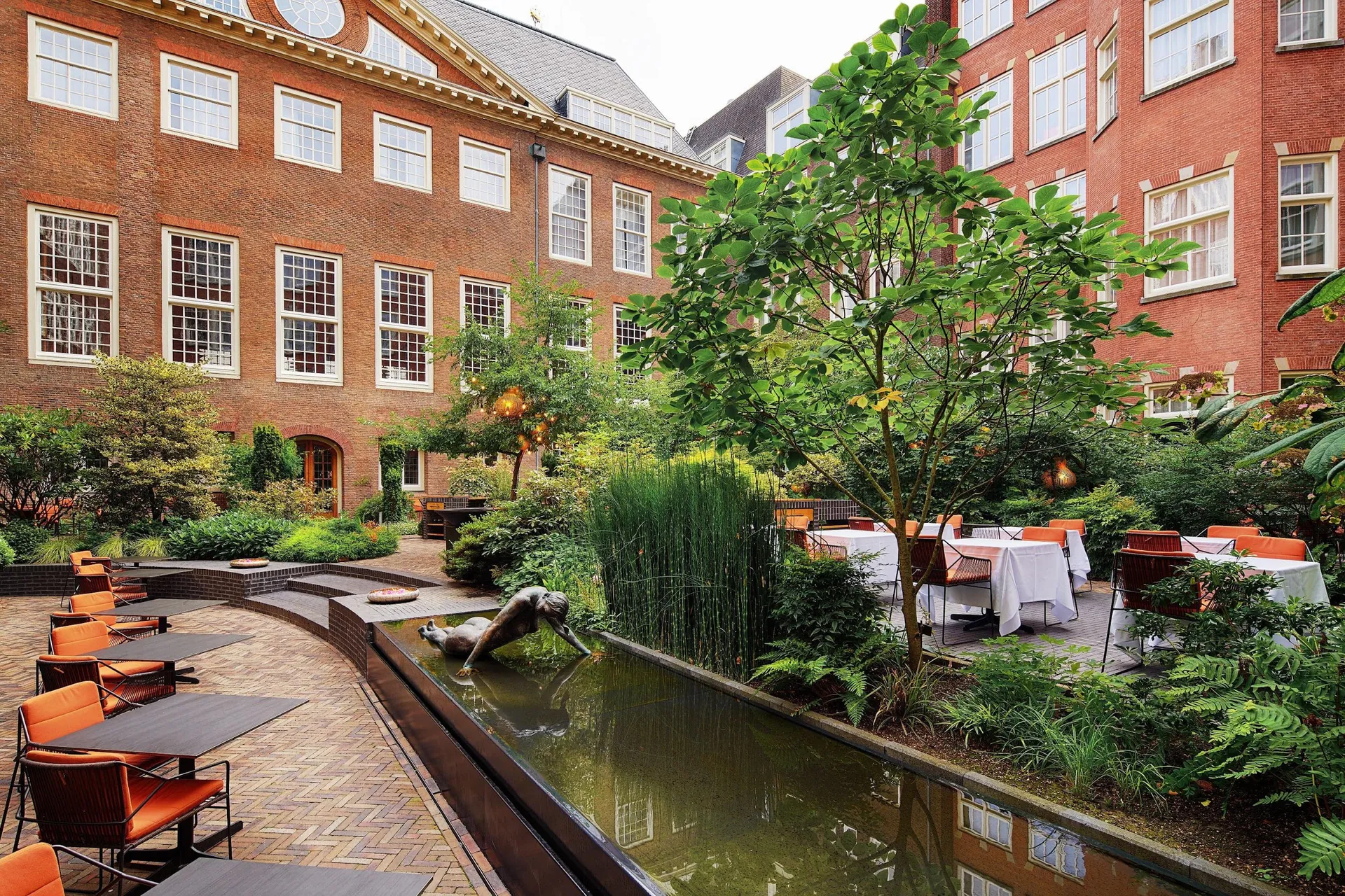 A leafy inner garden with a pond and terrace seating between brick wings.