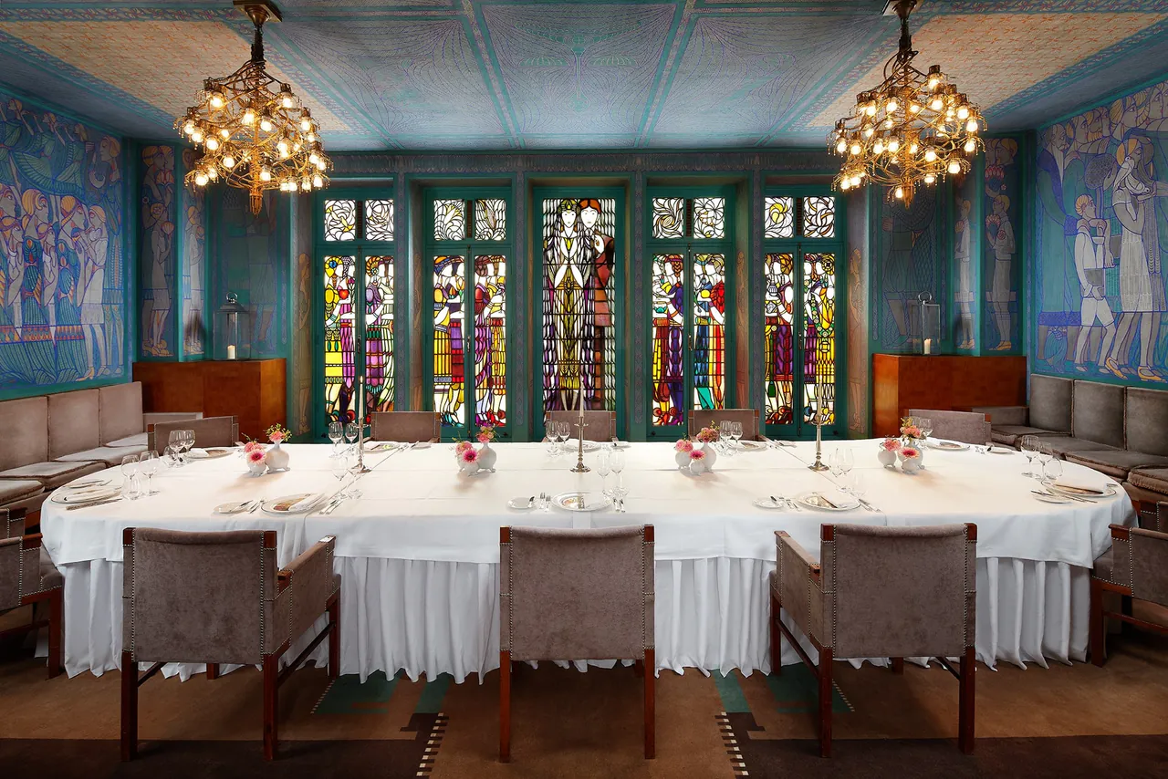 A long banquet table under chandeliers and stained glass windows.