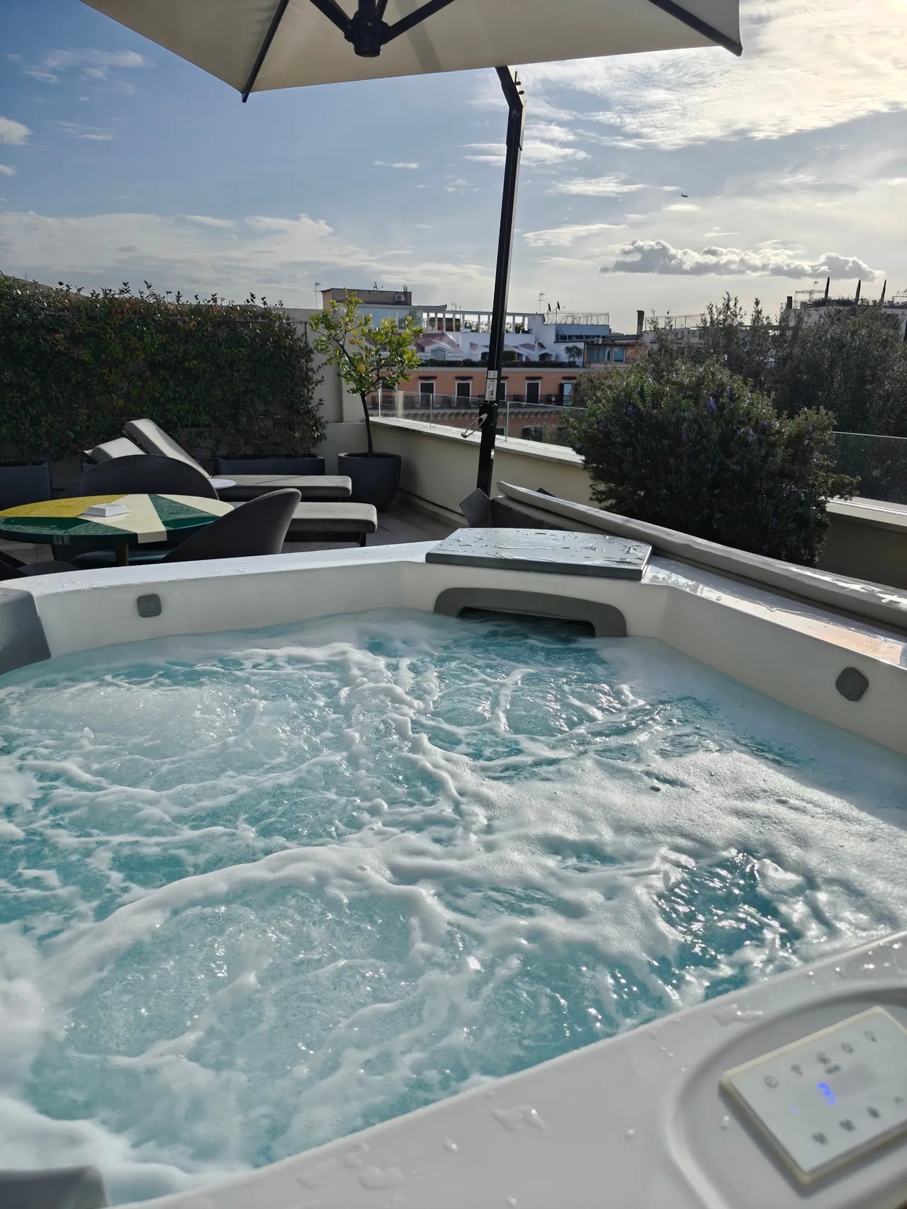 A bubbling hot tub on a terrace with a parasol and views over the rooftops.