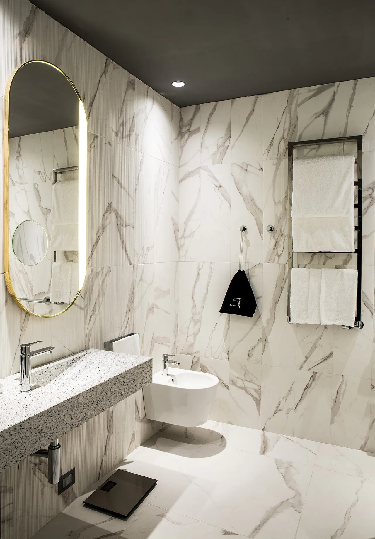 A white marble bathroom with an oval mirror and a walk-in shower.