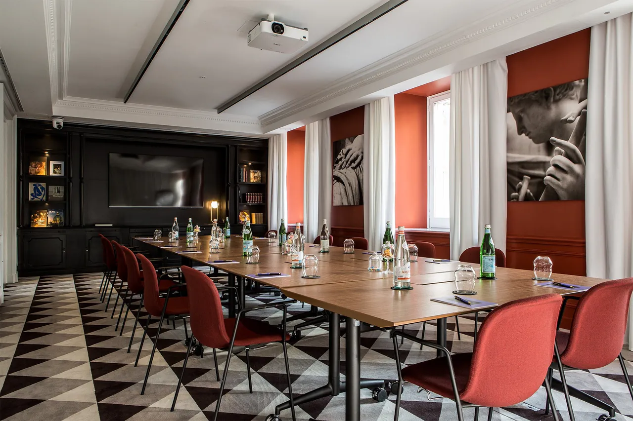 A meeting room with a long wooden table, red chairs and a chequered floor.