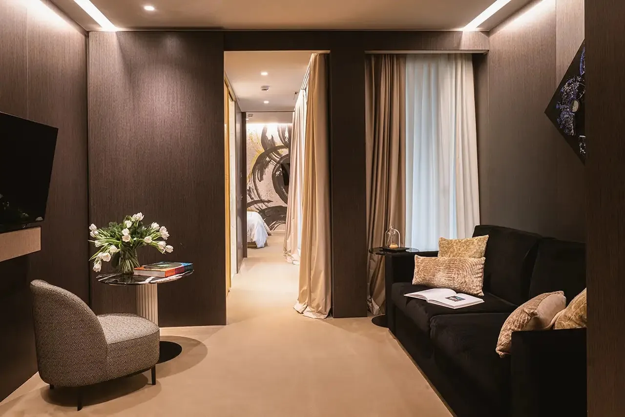Suite sitting area with a dark sofa, armchair and fresh flowers.