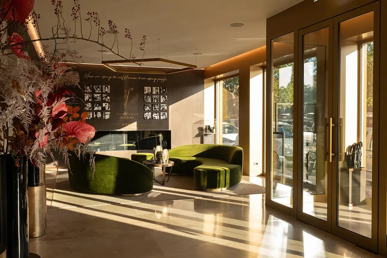 Sunlit lobby with green velvet sofas and tall glass doors.