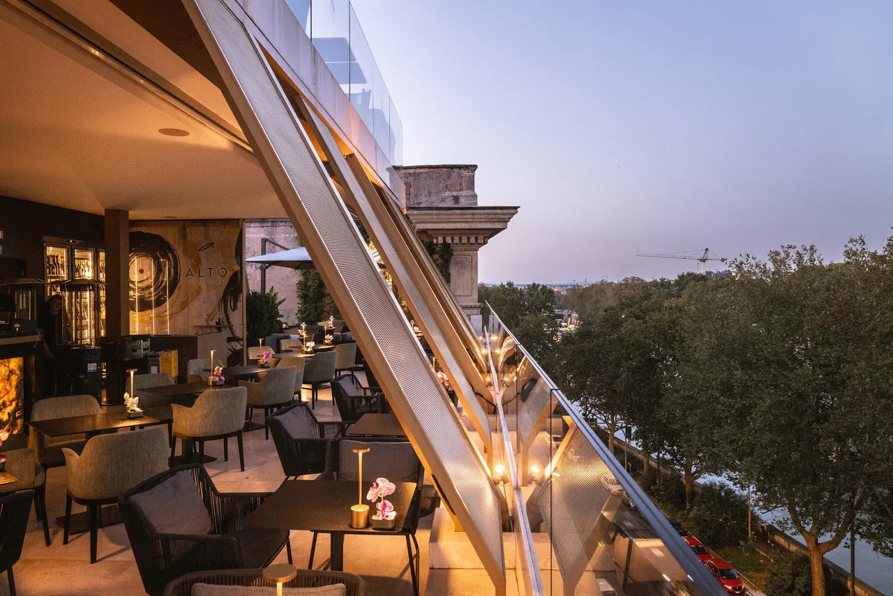 The rooftop restaurant glowing at dusk above the tree lined river.