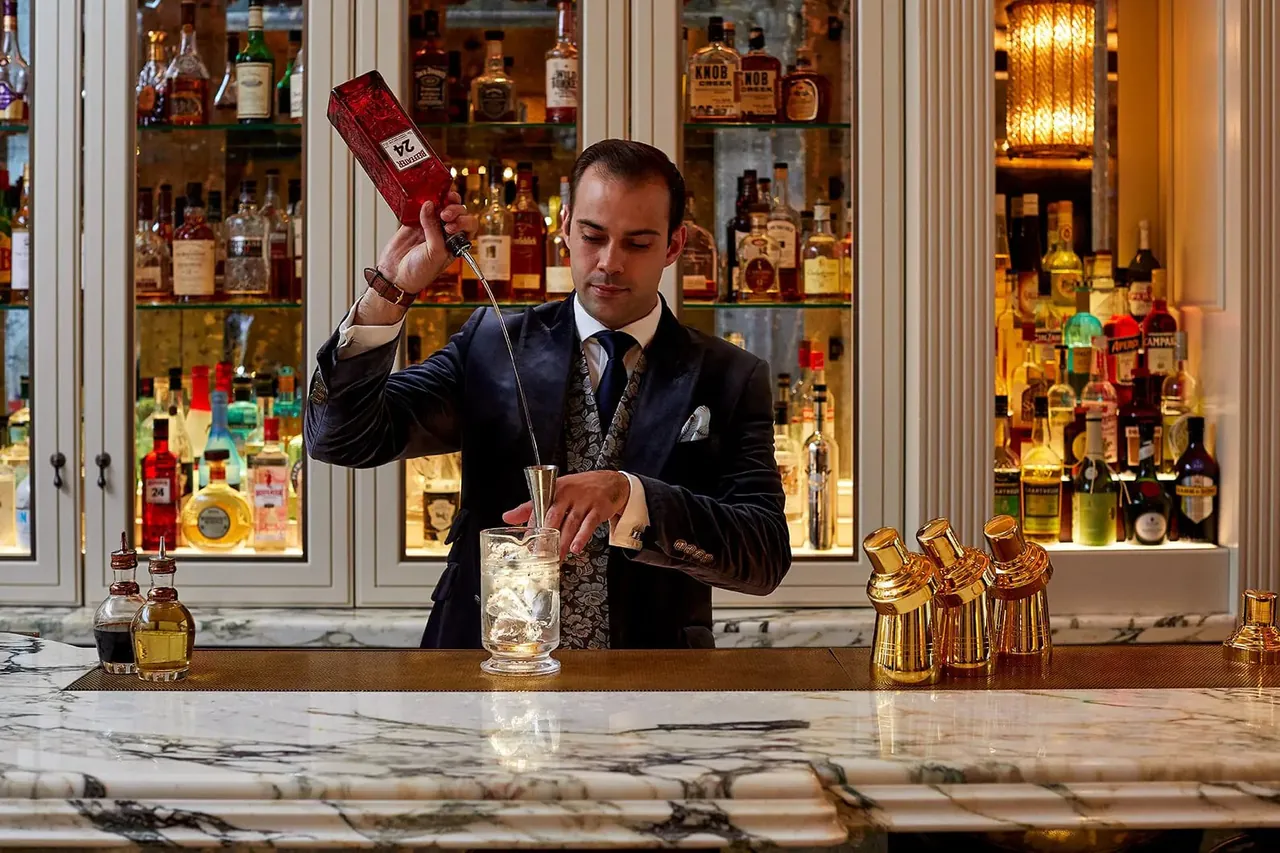 A bartender mixes a cocktail in front of a wall of bottles.