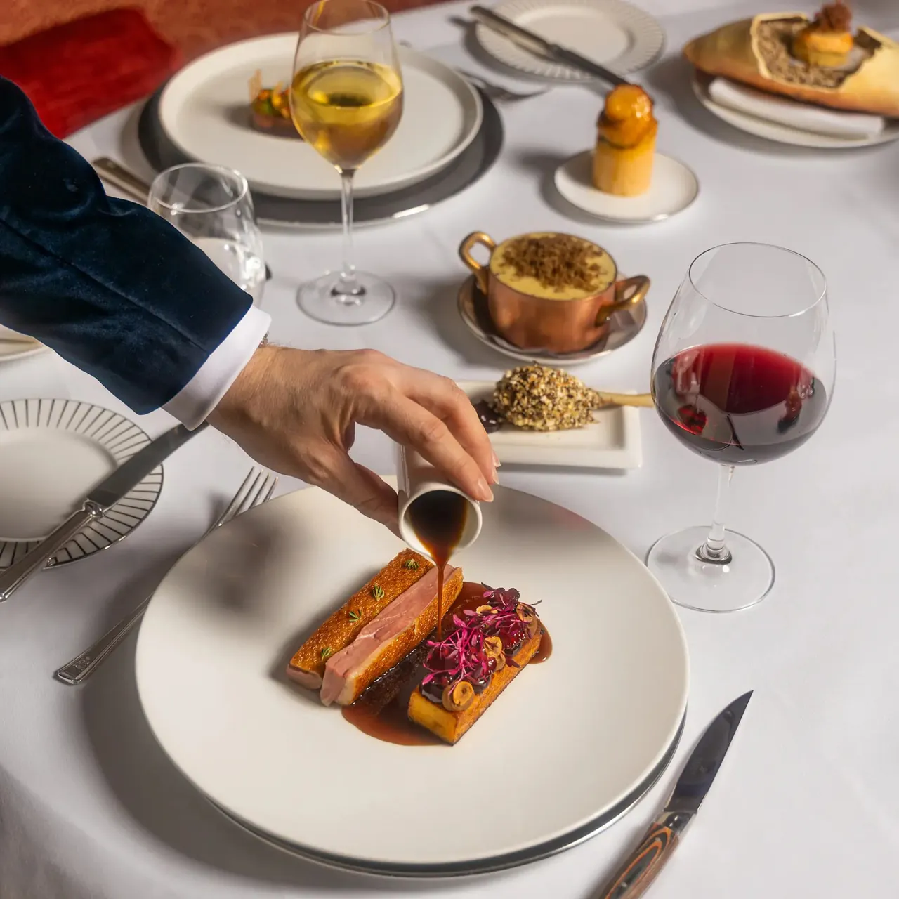 A waiter pours sauce over a plated dish in the restaurant.