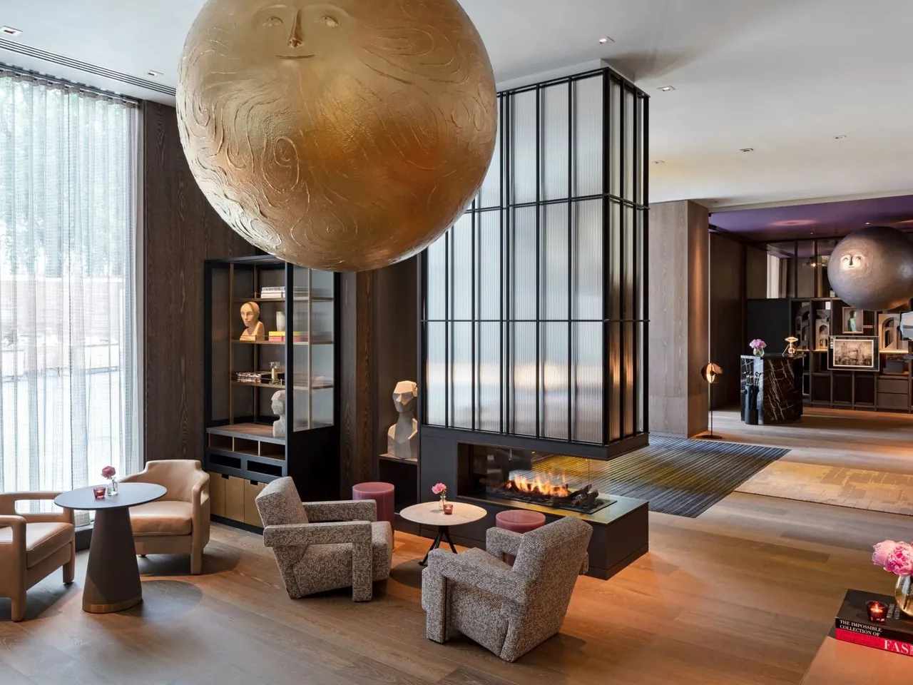 The lobby with a large golden sun sculpture, a fireplace and armchairs.