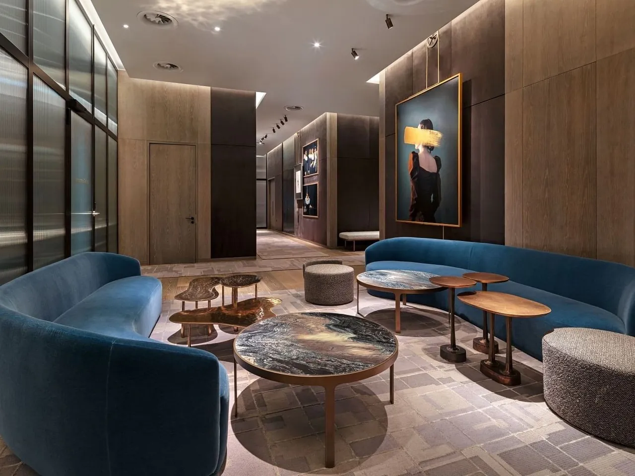 A lounge with curved blue velvet sofas, marble tables and modern art.