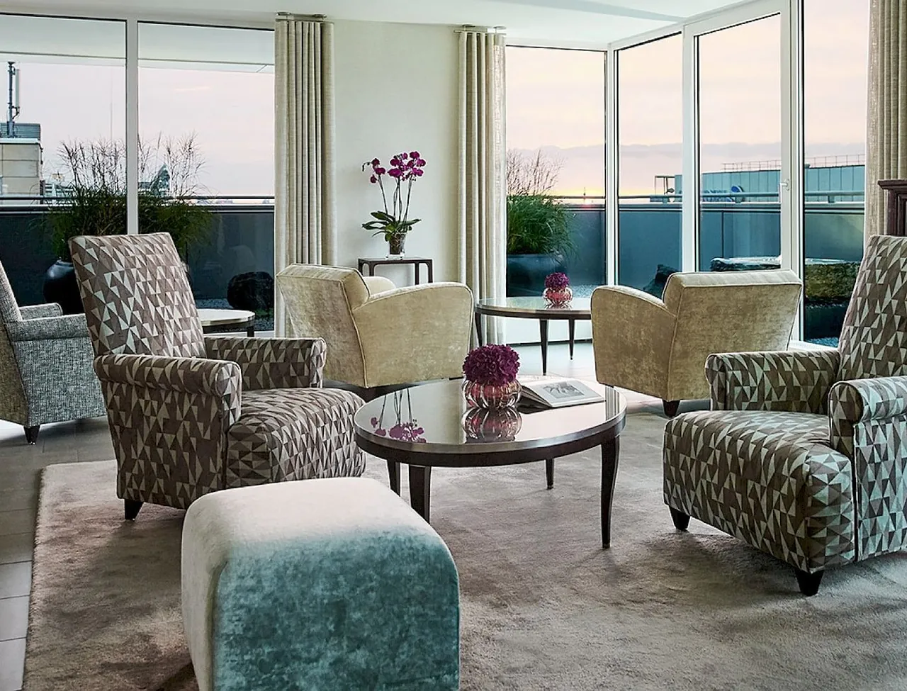A bright suite lounge with patterned armchairs and a terrace beyond the windows.
