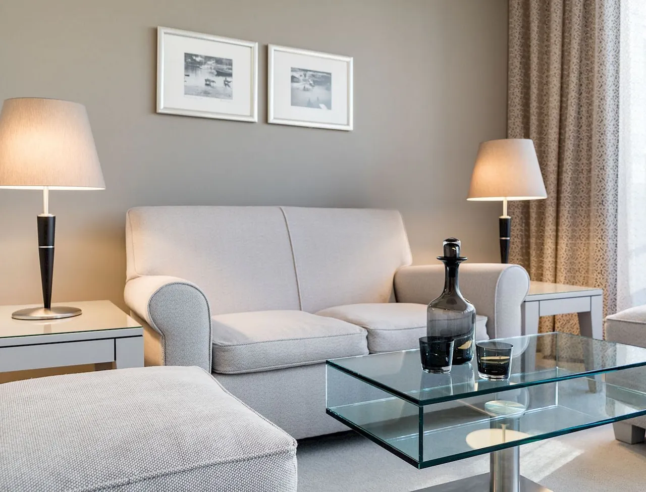 A suite sitting area with a white sofa, glass table and soft lamps.