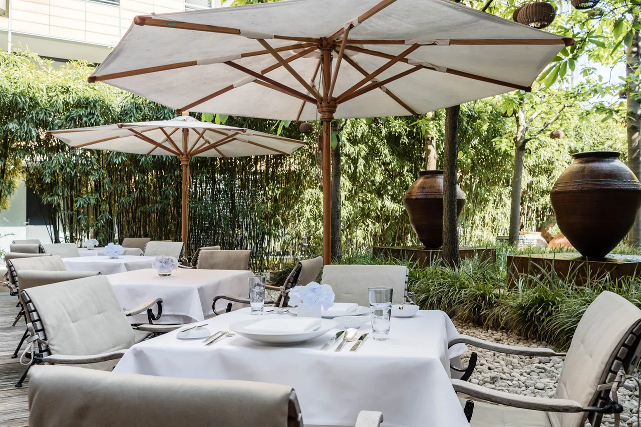 A garden terrace with white parasols and set tables among plants.