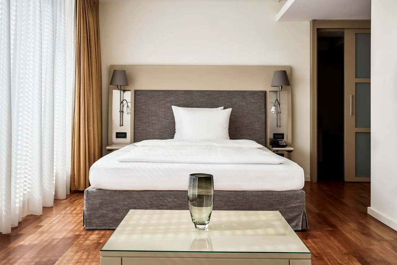 A calm bedroom with a white bed, wooden floor and walnut furniture.