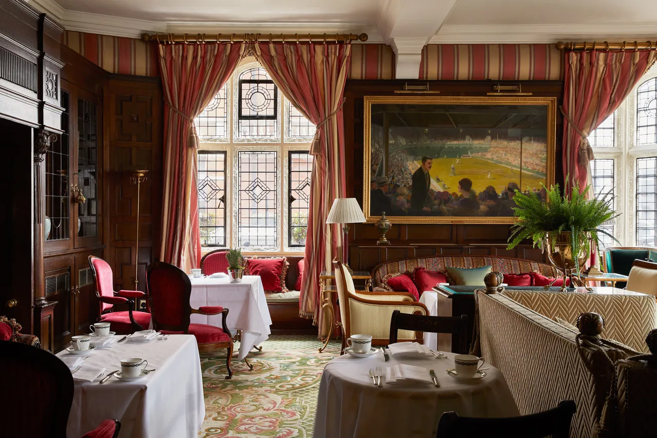 A lounge with red drapes, leaded windows and a large oil painting above tables set for tea.