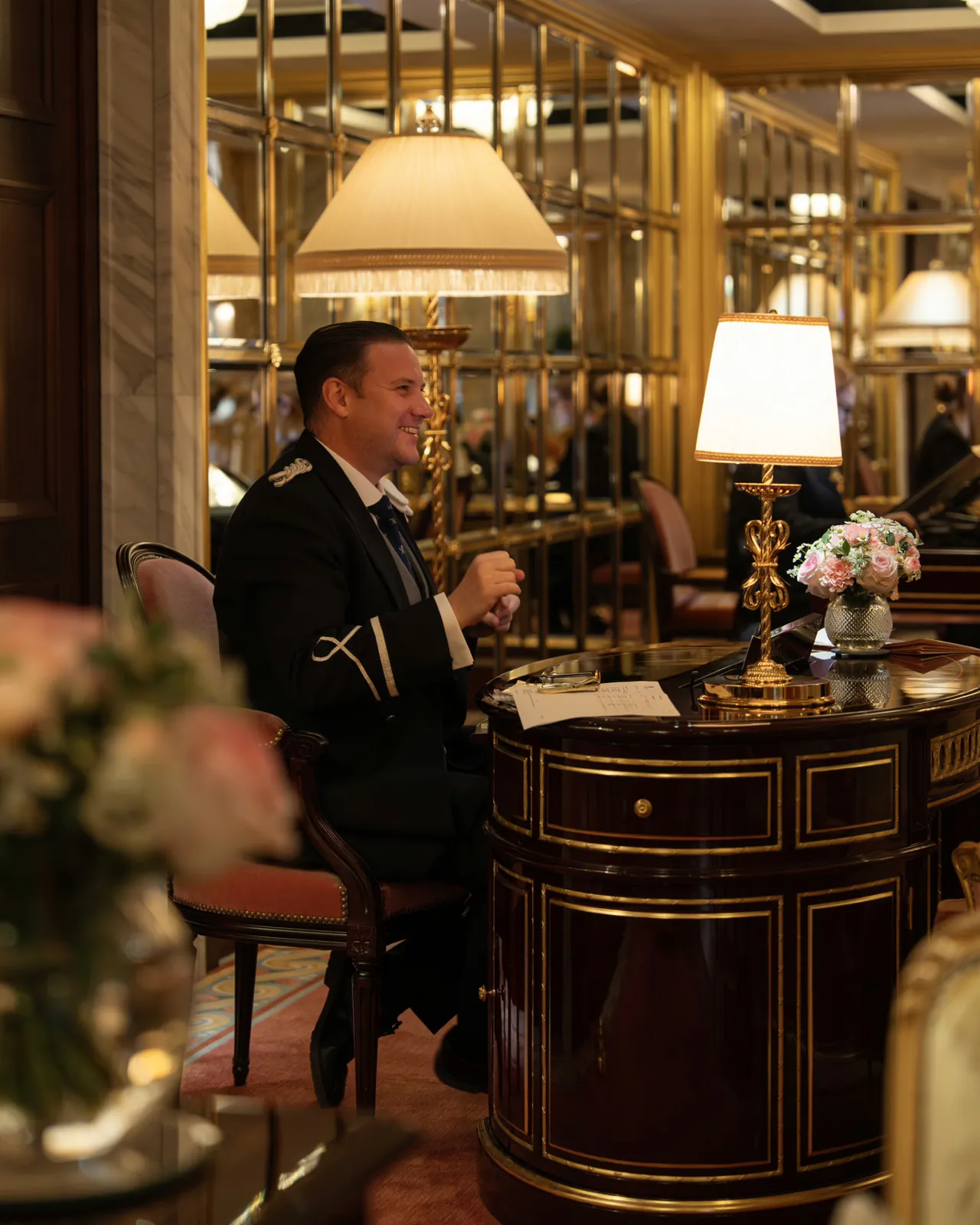 A host in a dinner jacket at a mirrored bar lit by table lamps.