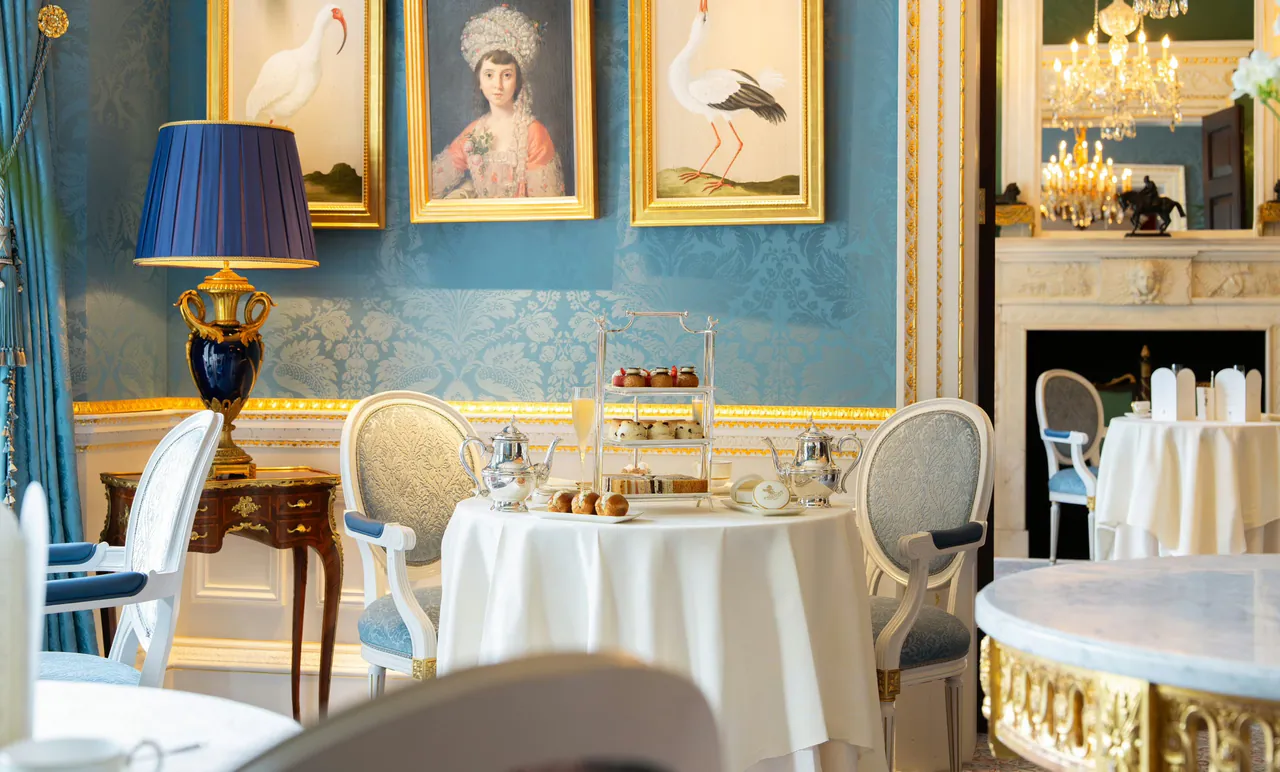 A blue-walled salon with tables laid for afternoon tea.
