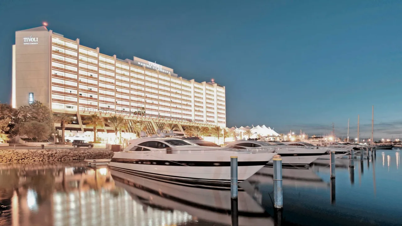Tivoli Marina Vilamoura hotel tower lit at dusk behind motor yachts moored in the marina