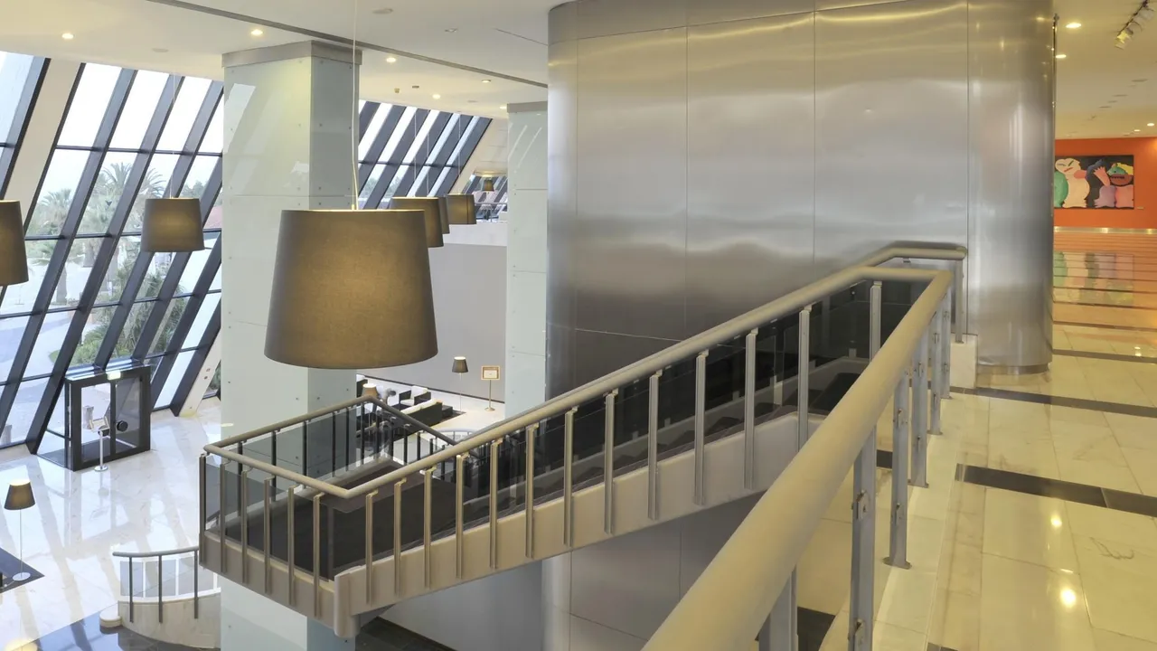 Lobby at Tivoli Marina Vilamoura with a steel-clad staircase, drum pendant lamps and slanted glass walls