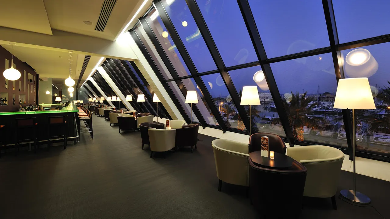 Lounge bar at Tivoli Marina Vilamoura with slanted floor-to-ceiling windows overlooking the marina at dusk