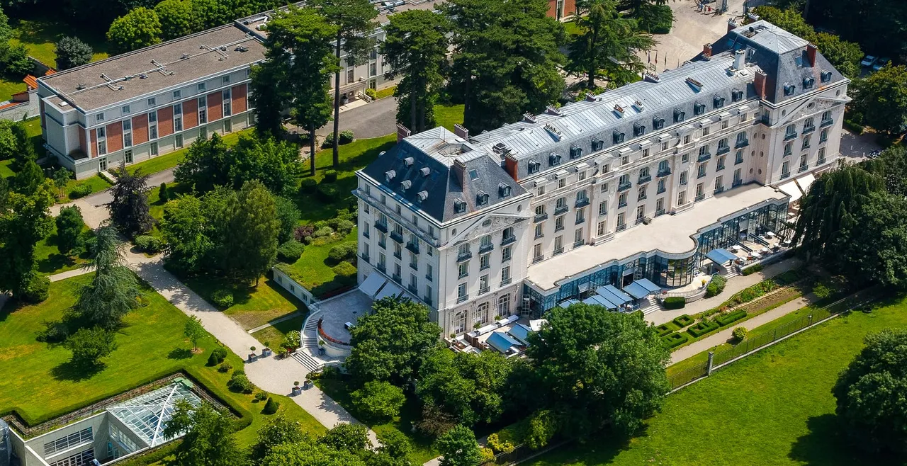 Aerial view of the white facade of Waldorf Astoria Versailles, Trianon Palace, set among lawns and trees