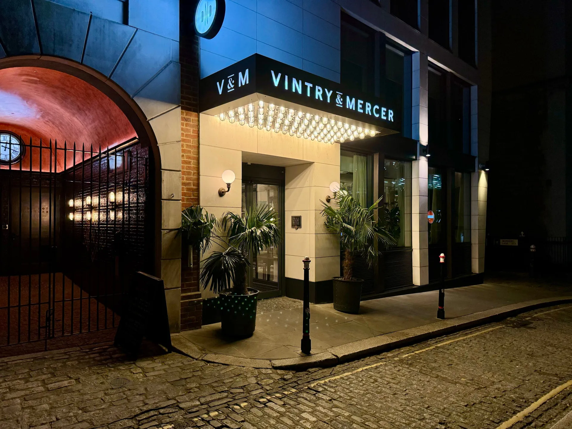 The lit entrance of Vintry and Mercer on a cobbled City street at night.