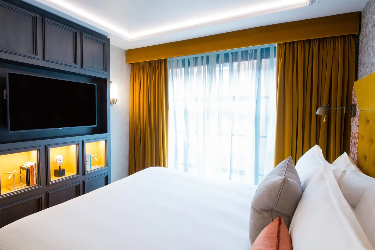 A bright bedroom with mustard curtains and a built-in unit with warm lighting.